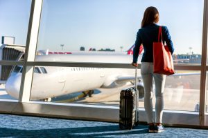 Traveler with suitcase in airport waiting for holiday travel with her carry-on suitcase next to her.