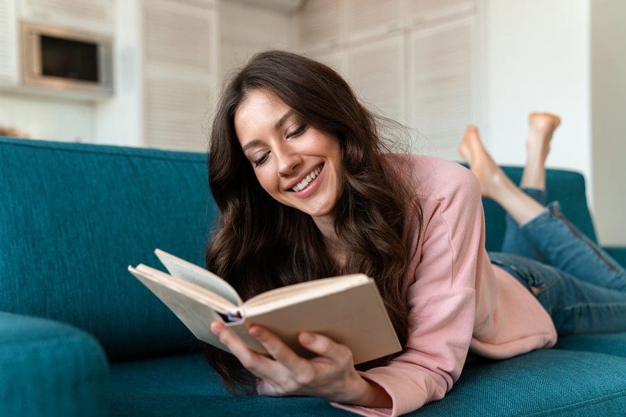 A woman laying on the couch reading a book.